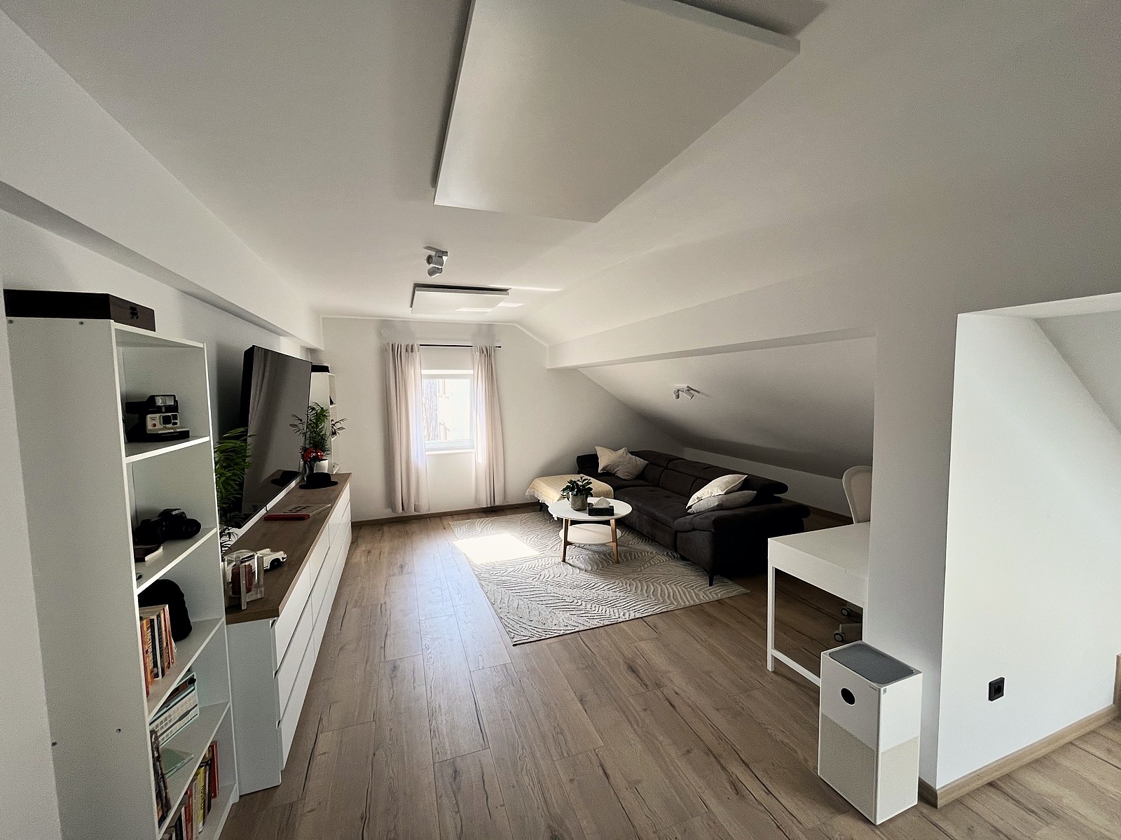 The living room in late-afternoon light — dark sofa, round coffee table, and the sloped ceiling