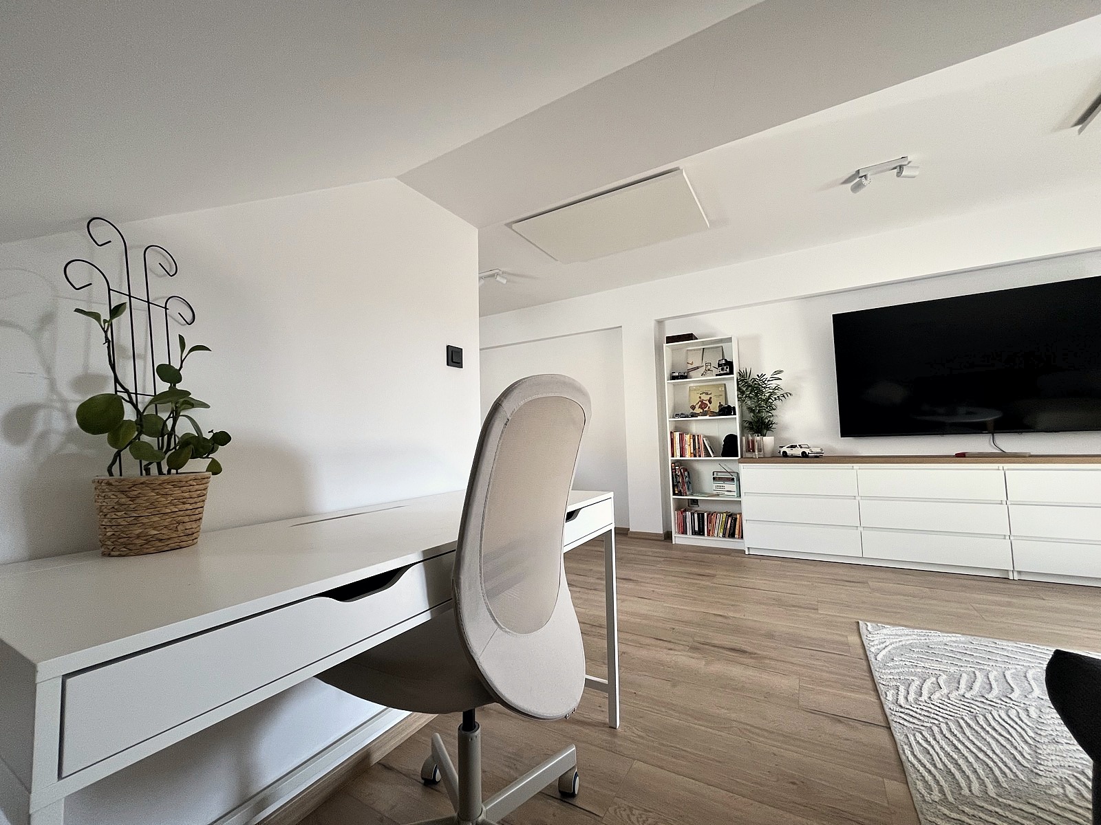 Dedicated workspace with white desk, ergonomic chair, plant, and TV unit visible